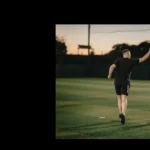 Two veterans in sports attire high-five on a soccer field at dusk. The man on the left is wearing black shorts and a black shirt, while the man on the right sports a striped jersey. The background reveals blurred trees against a warm sky transitioning to night. © Powerleague
