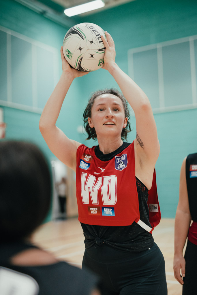 A netball player wearing a red bib labeled 