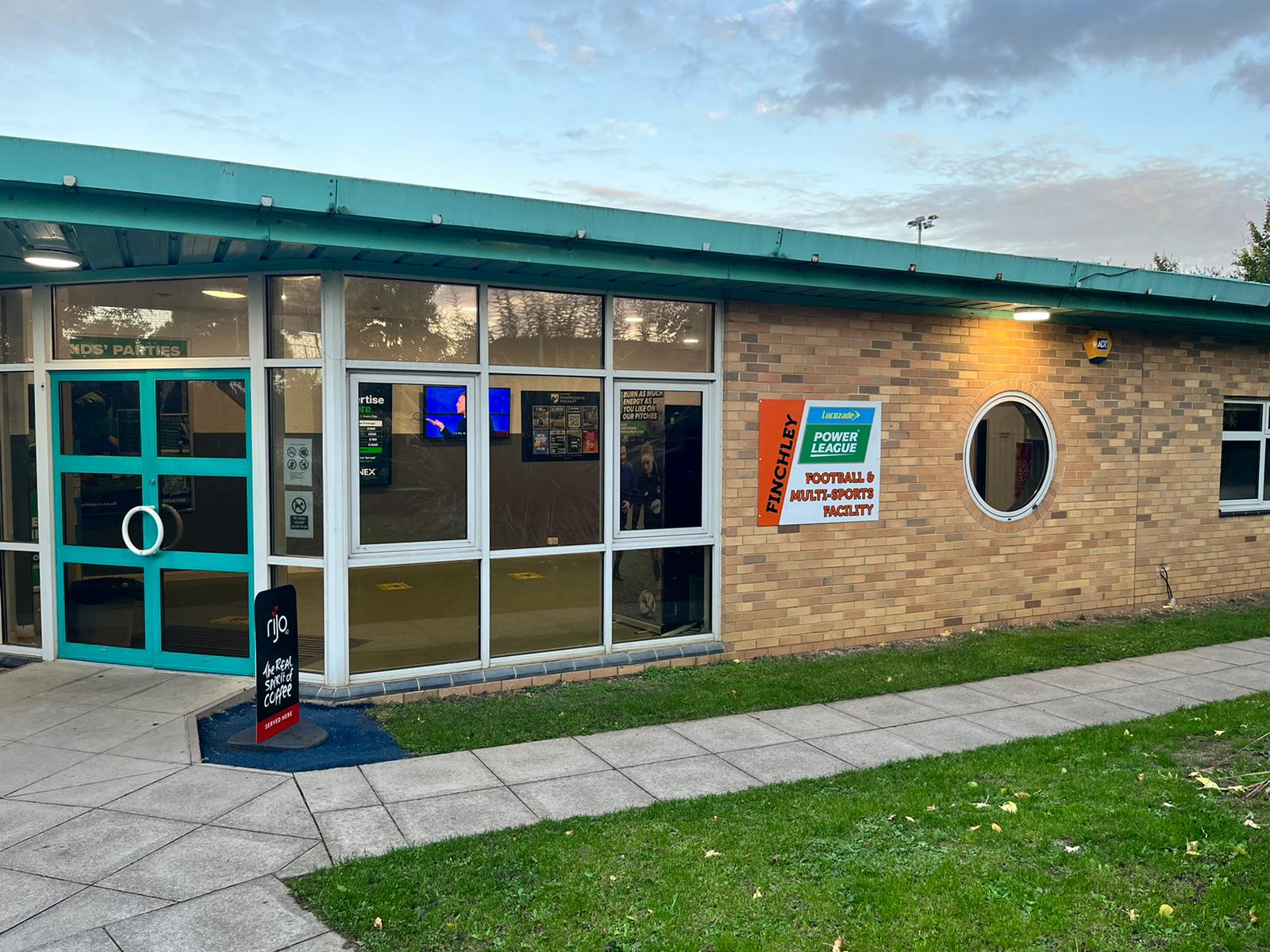 The exterior of a brick sports facility boasts large windows, signs for 