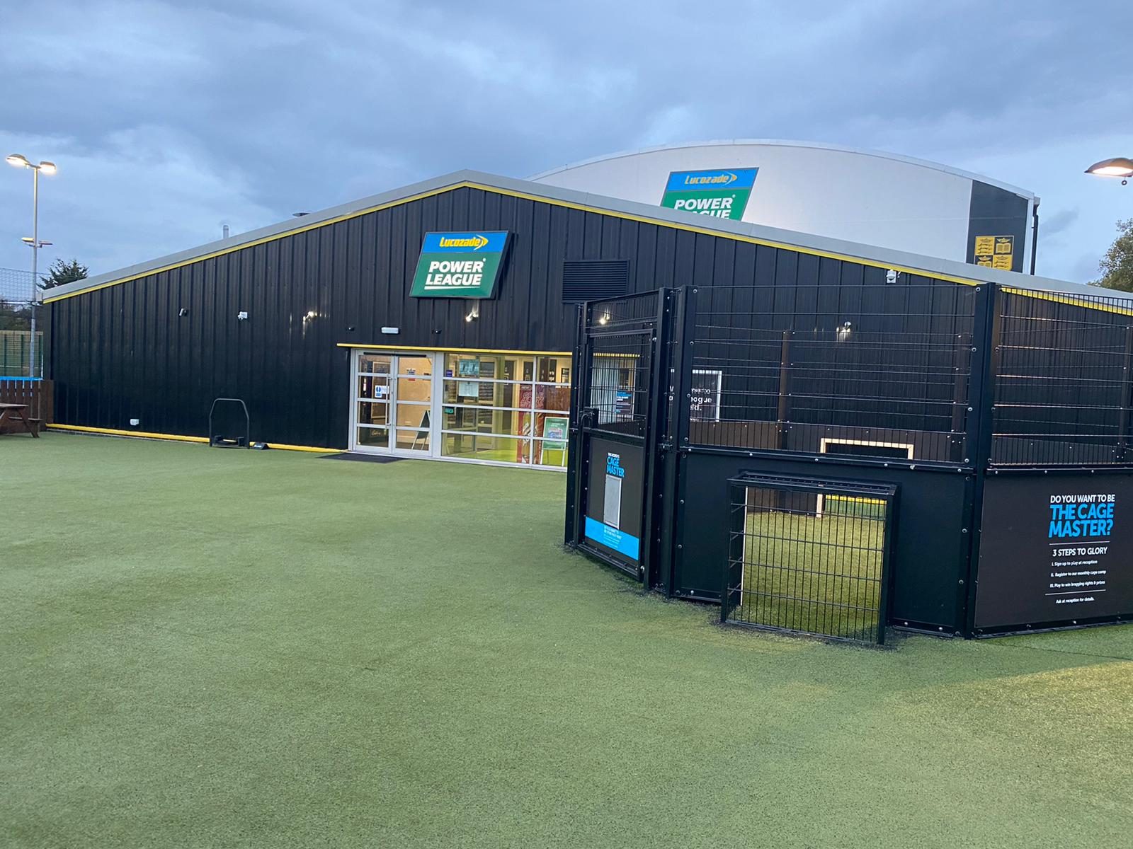 Exterior view of a Powerleague sports facility showcasing a modern building with a glass entrance and black metal facade. The sign above reads 