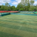 A multi-purpose outdoor sports facility with several artificial turf fields enclosed by green barriers. Each field has goalposts and floodlights, perfect for local football leagues. Trees frame the area under a cloudy sky in the background. © Powerleague